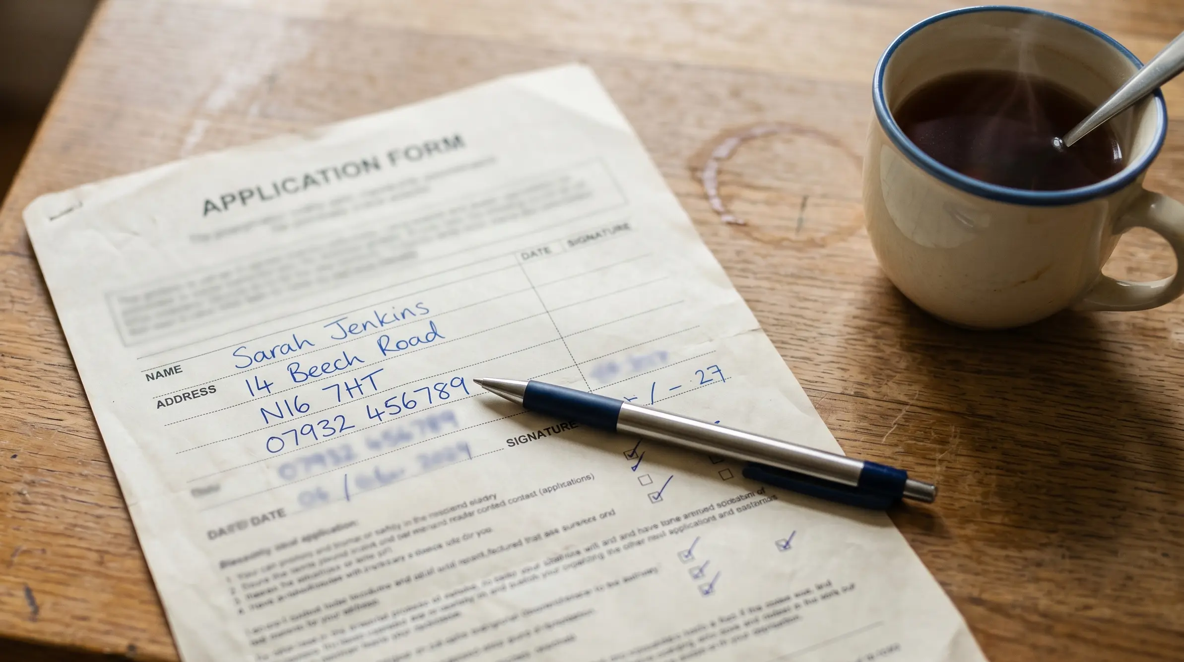 Worn paper form partially filled in with blue ink, a pen resting across it on a wooden kitchen table